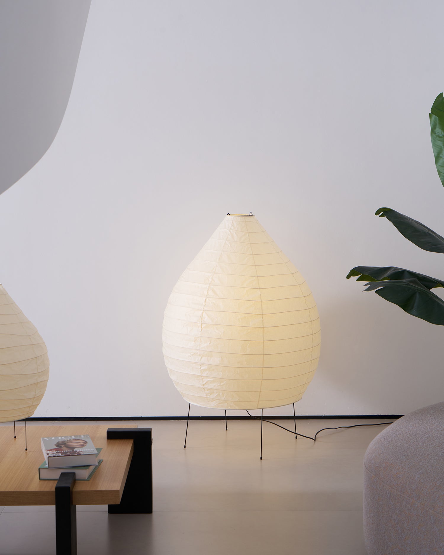 Illuminated Akari 23N teardrop floor lamp in living area with stacked books on side table