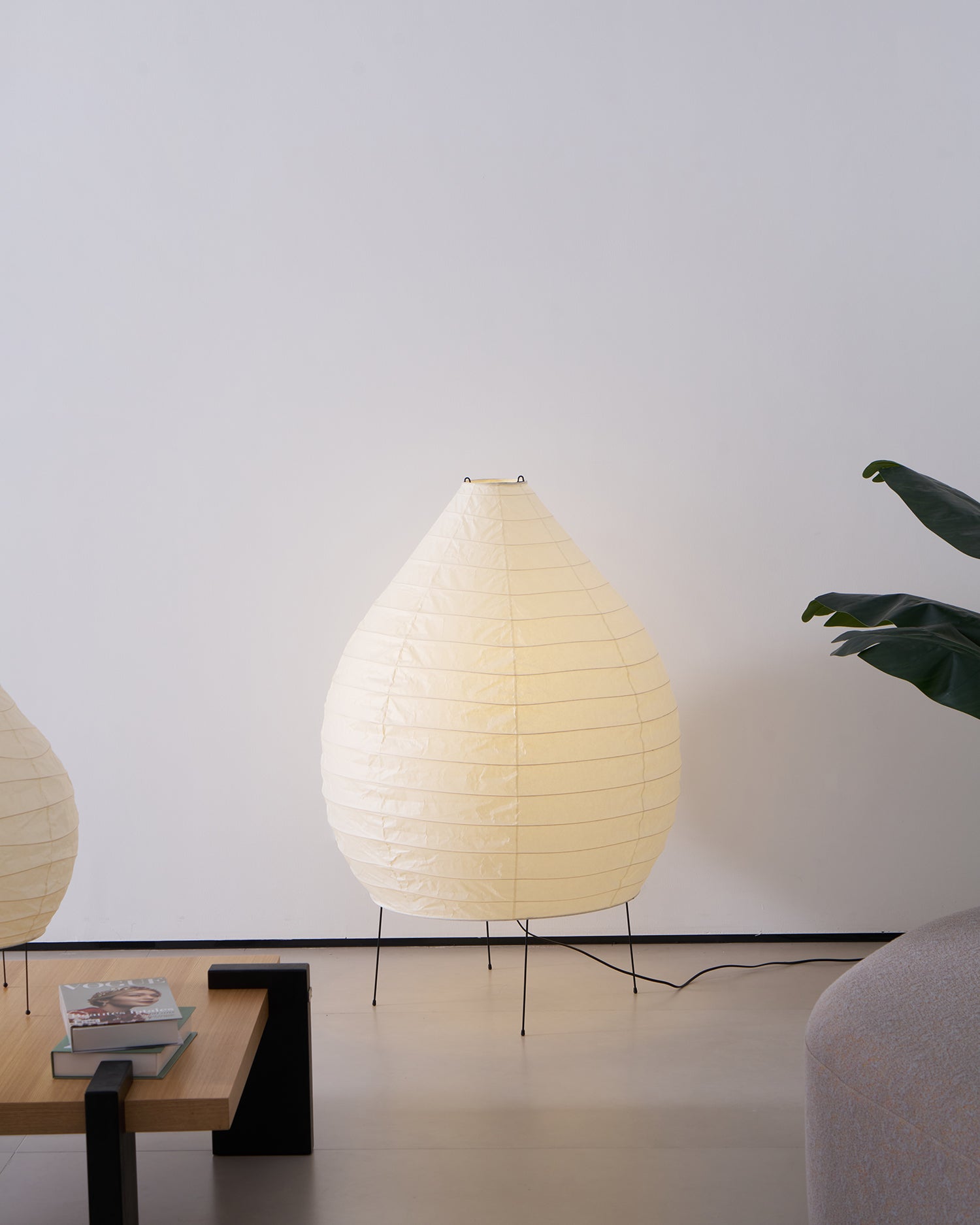 Akari 23N teardrop floor lamp three-quarter view in minimalist space with black metal legs and books