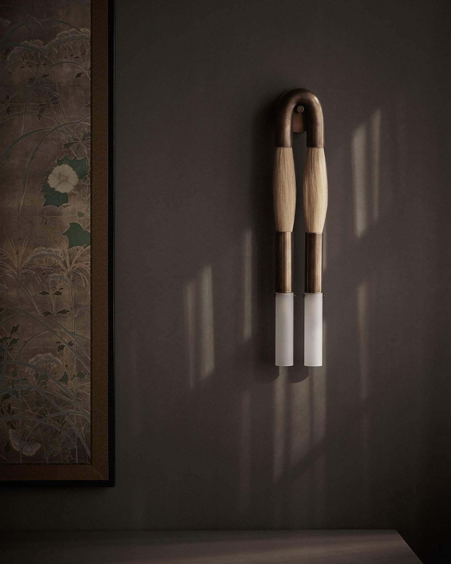 Branwick sculptural wall sconce mounted on dark brown entryway wall beside traditional art, modern lighting design for oriental interior