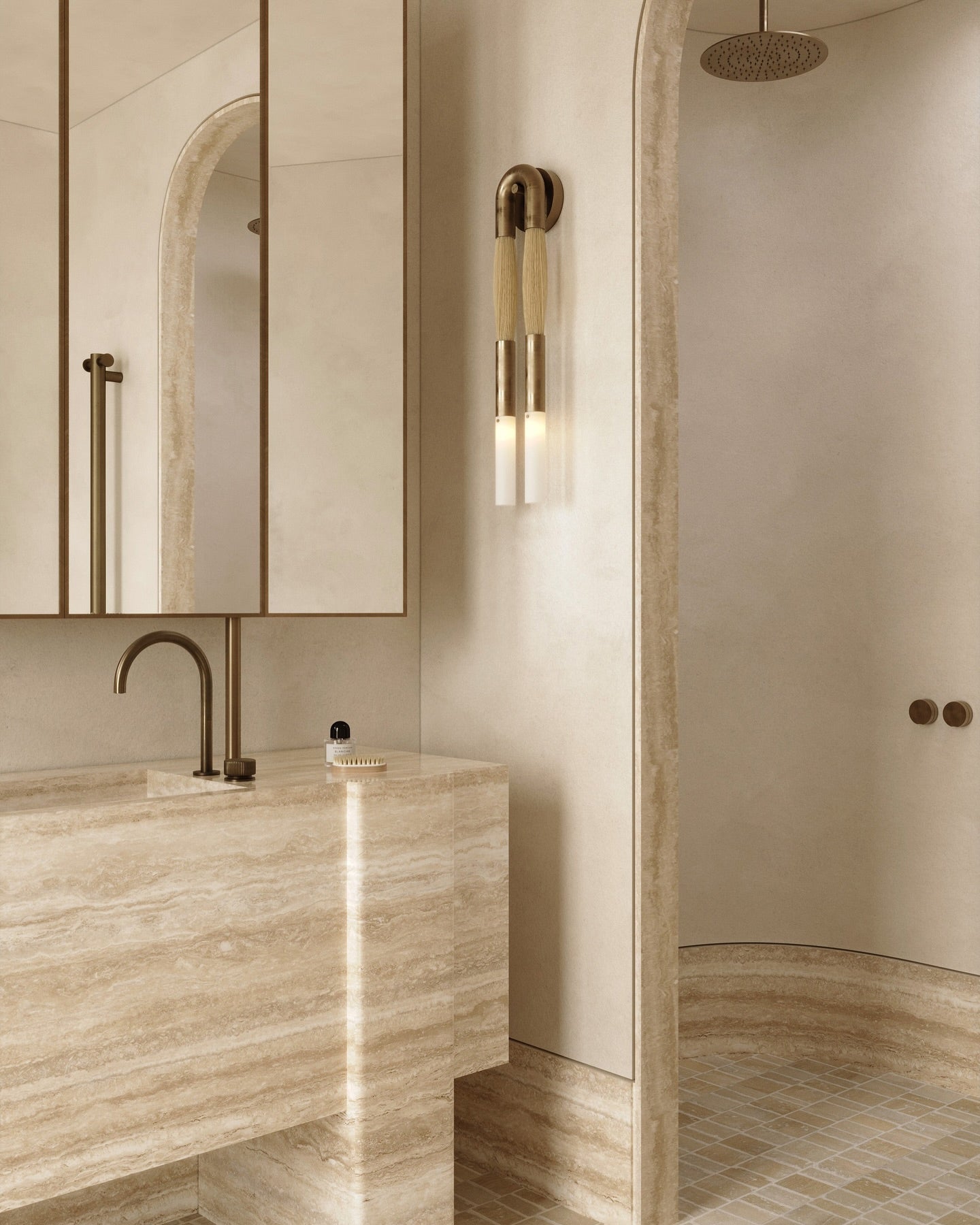 Single Branwick modern wall sconce installed above bathroom vanity in minimalist travertine space with warm accent lighting