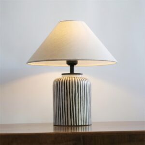Black and white striped ceramic table lamp with neutral fabric shade on wooden tabletop in minimalist interior