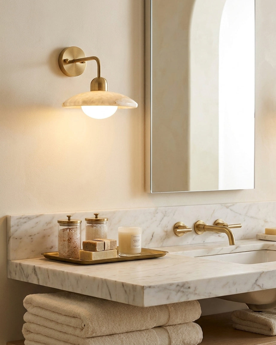 Carolia alabaster wall sconce coordinating with brass faucet hardware above marble bathroom vanity