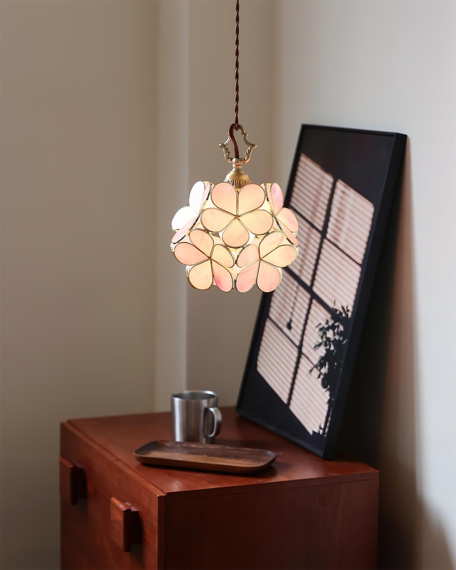 Peach-pink stained glass pendant light illuminated above home dresser with wall art