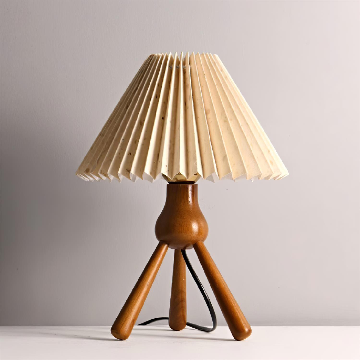 Cream pleated fabric shade on solid wood tripod table lamp with black power cord, front view