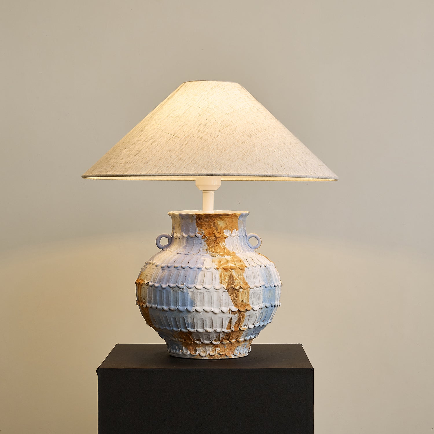 Illuminated Grazie ceramic table lamp displaying warm ambient light diffused through textured linen shade with marbled blue-brown handcrafted pottery base glowing