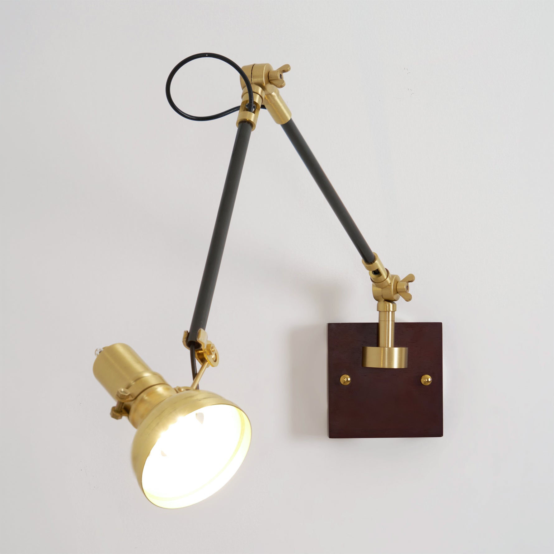 Kane swing arm wall lamp low-angle front view with lit lampshade and dark walnut mounting base
