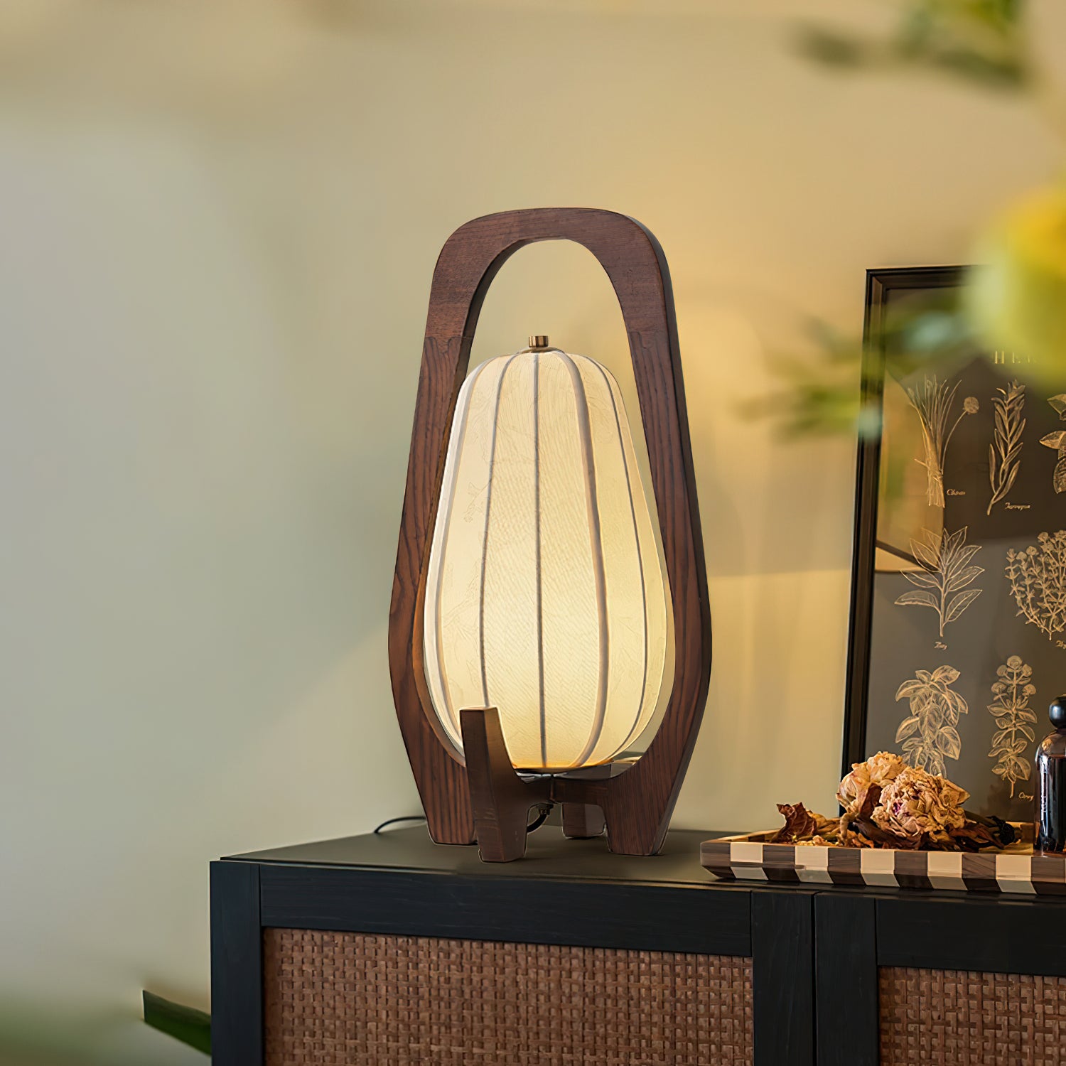 Arched wooden table lamp on dark rattan cabinet with wall art and decorative dried props, Scandinavian home interior