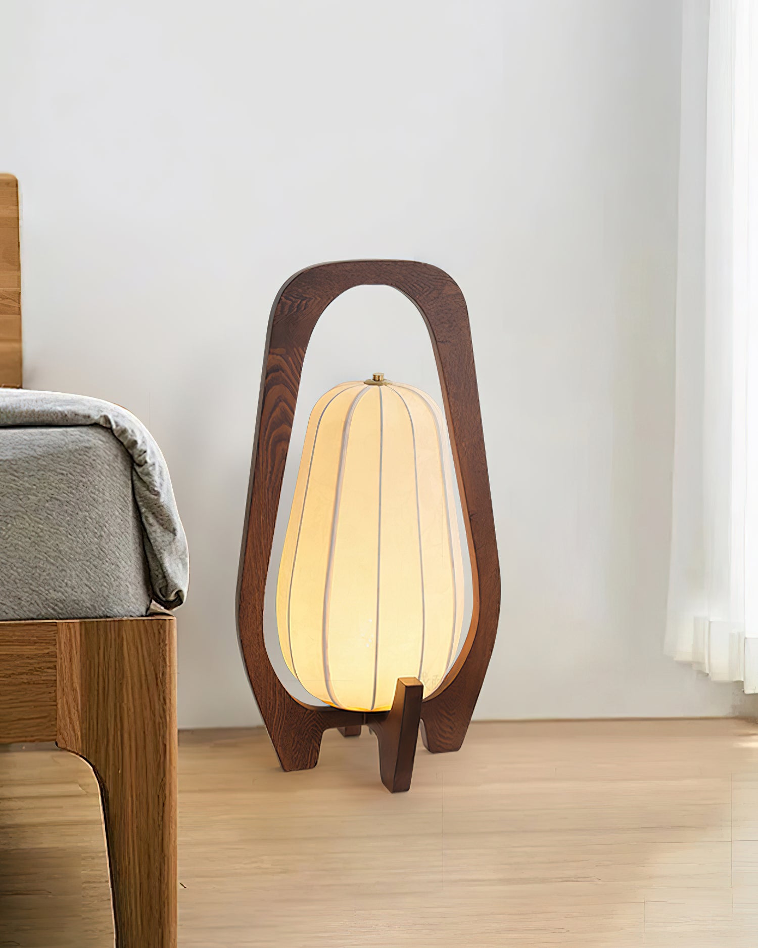 Wooden table lamp placed on bedroom floor beside wooden bed frame, neutral home decor setting with natural lighting