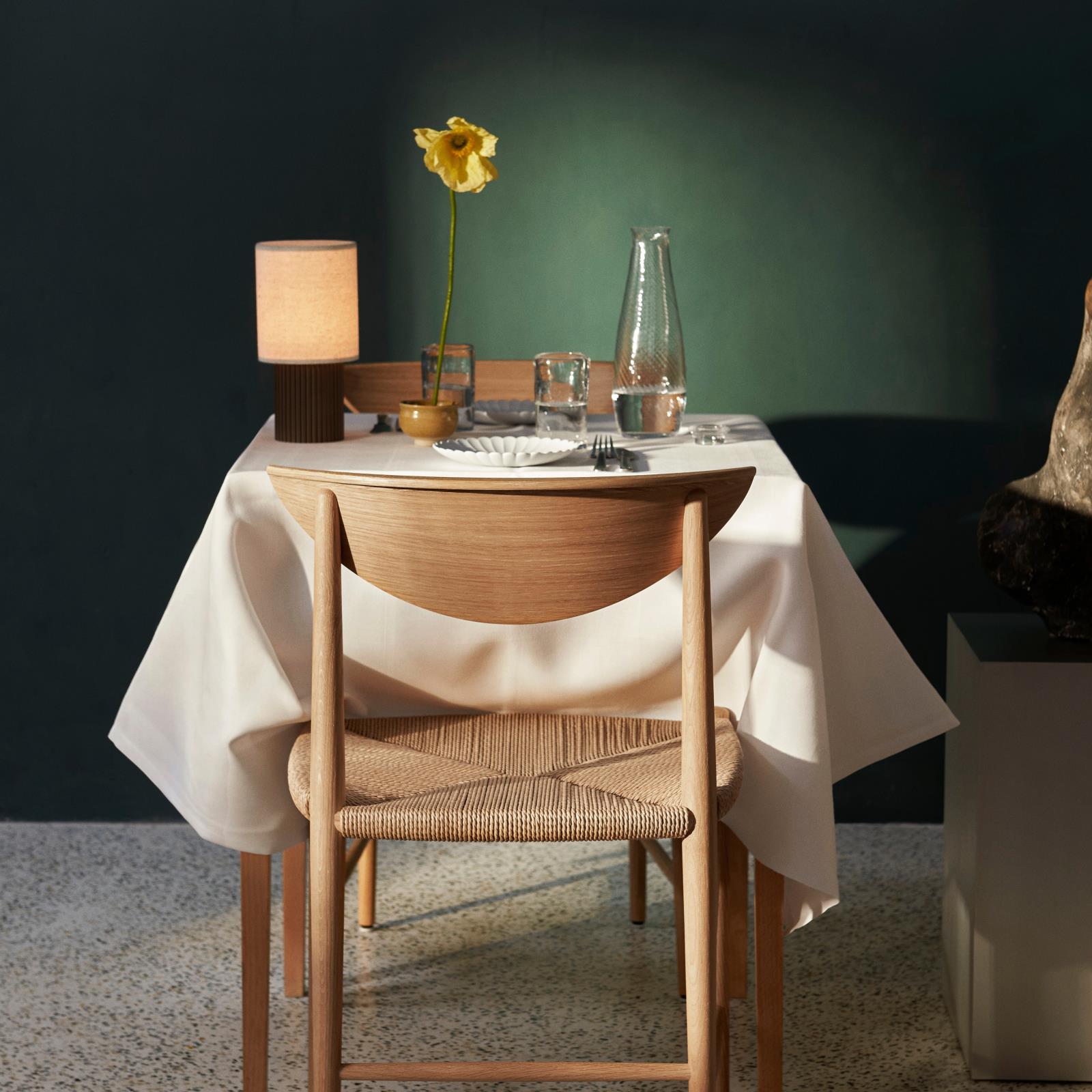 Lit minimalist table lamp creating warm ambient 3000K lighting in formal dining room, demonstrating cozy dinner atmosphere