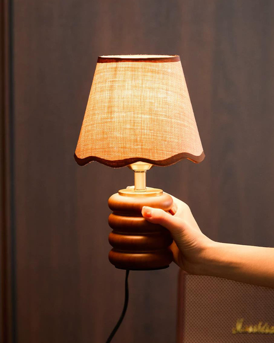 Close-up of Marlowe table lamp held by hand with warm glowing light against dark wood panel background