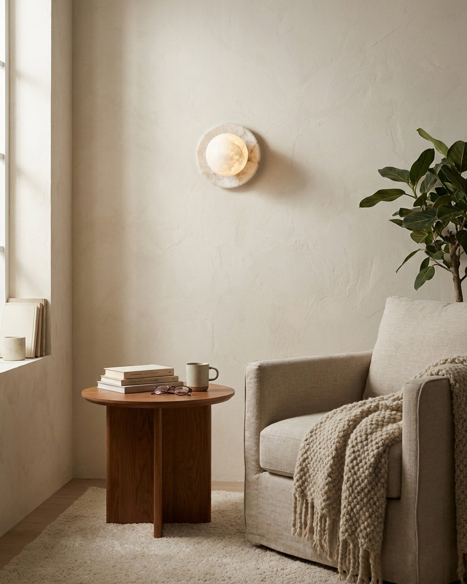Alabaster ball wall sconce paired with armchair and side table in cozy reading nook, warm glow ambient lighting