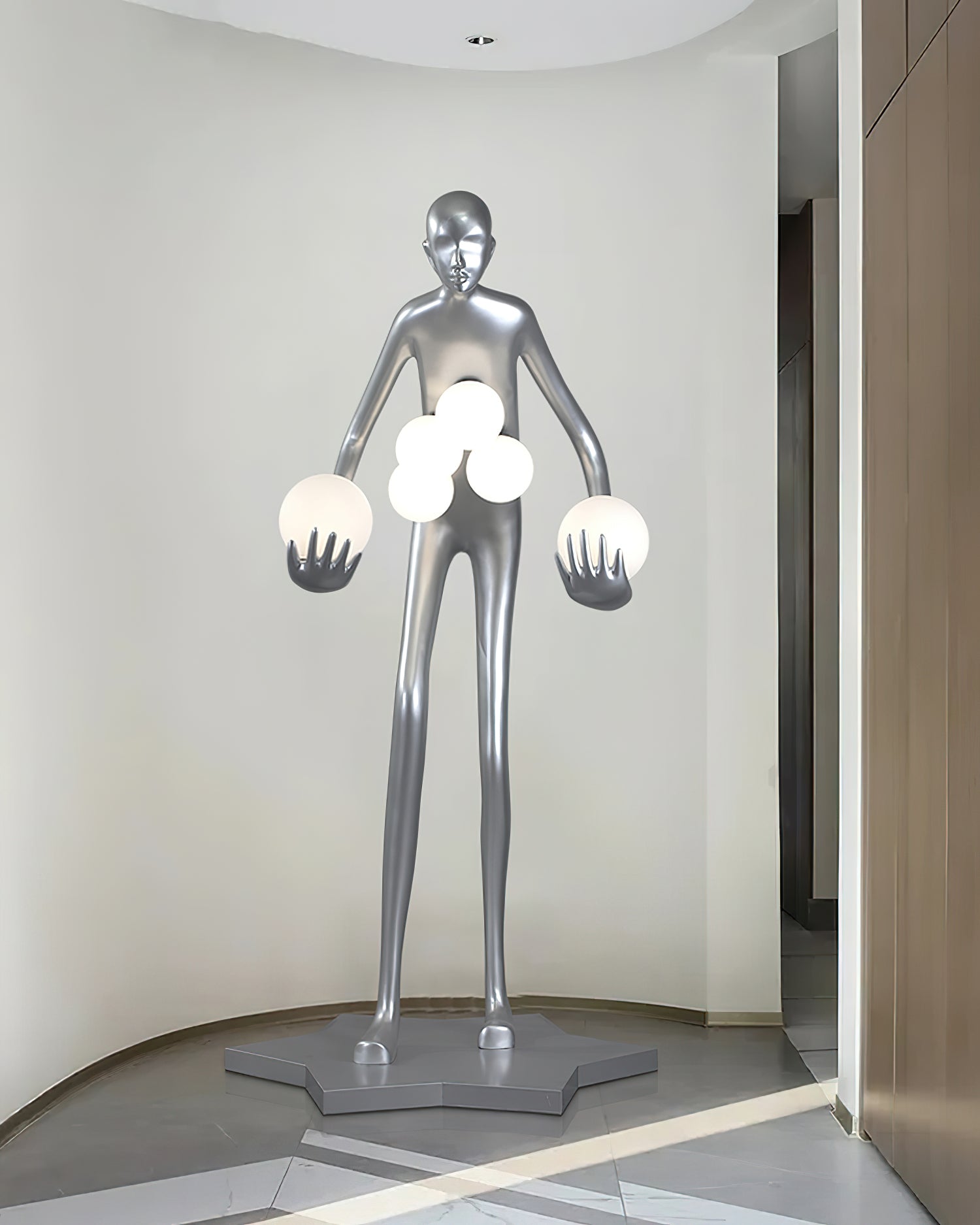 Silver sculptural floor lamp with human form and multiple frosted light orbs in minimalist white hallway space