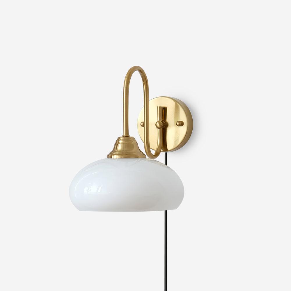 Textured glass plug-in wall sconce with gold brass base and white milk glass dome shade, front three-quarter studio view