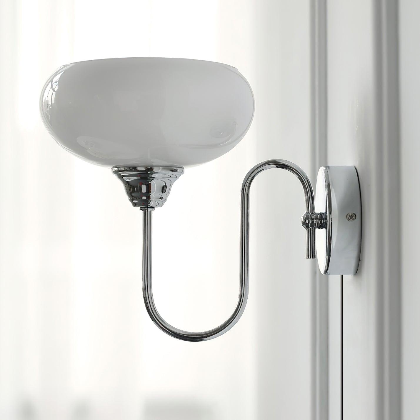 Modern plug-in wall light in chrome finish with gray textured glass shade, side view in bright indoor room with sheer curtains