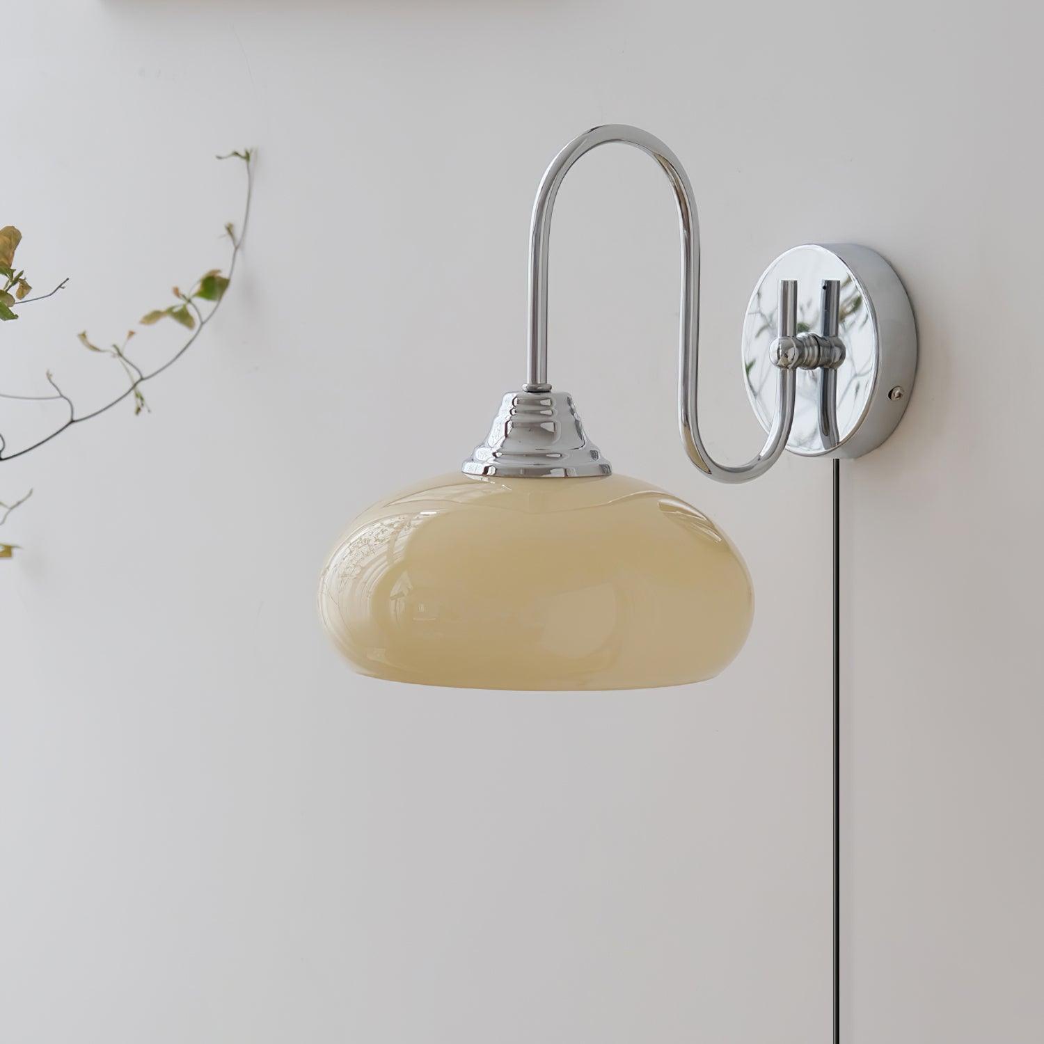 Damp-rated plug-in wall sconce with chrome base and beige amber textured glass shade, minimalist interior with plant decor