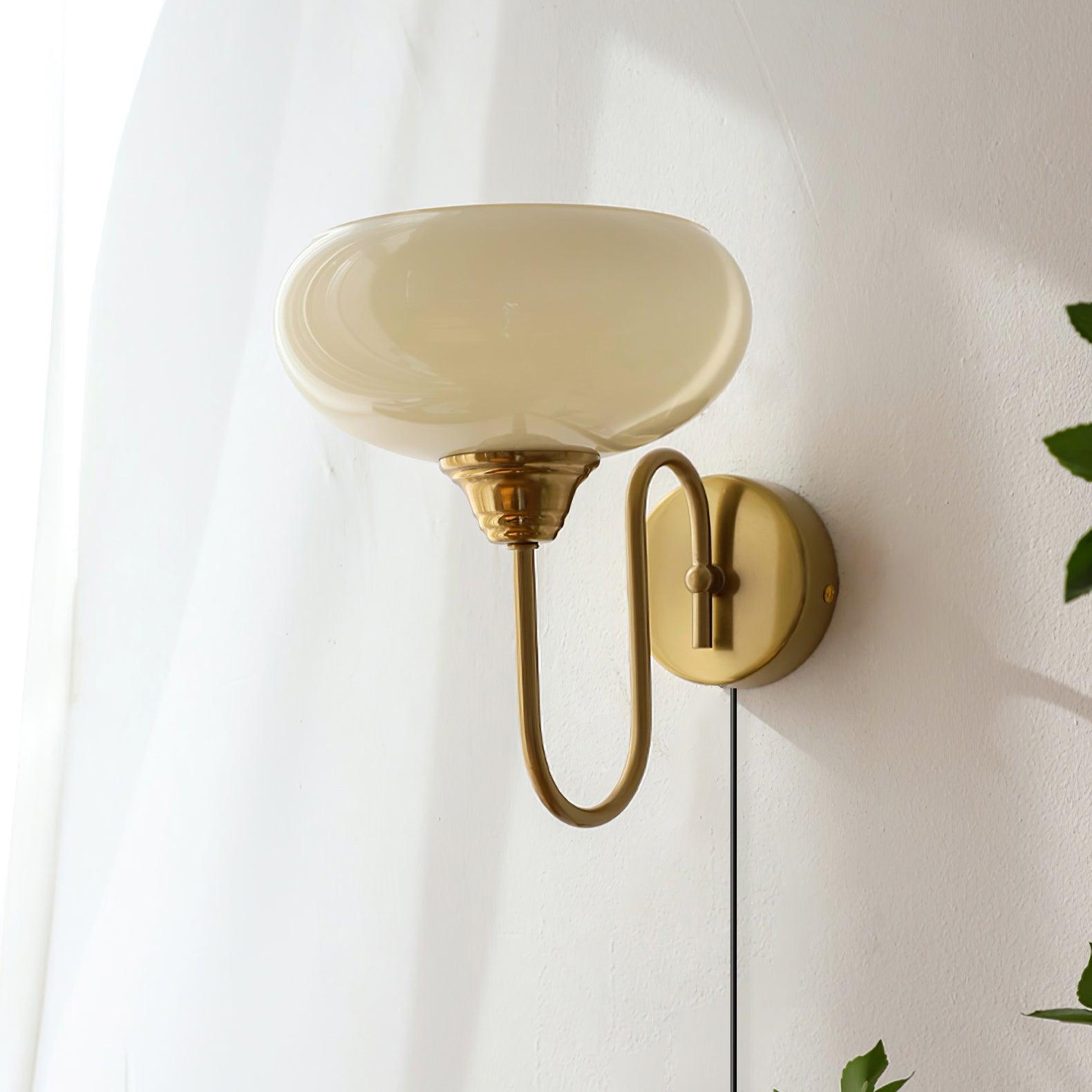 Vintage-style mid-century plug-in wall sconce with brass gold hardware and off-white amber glass shade, room with sheer window curtains