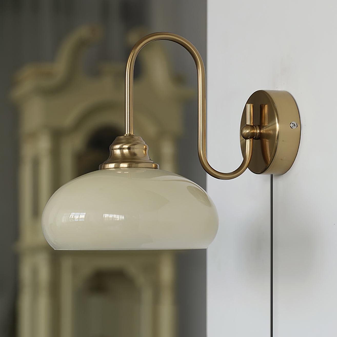 Textured glass wall sconce in gold brass finish with milky white glass dome, side view in indoor space with vintage furniture