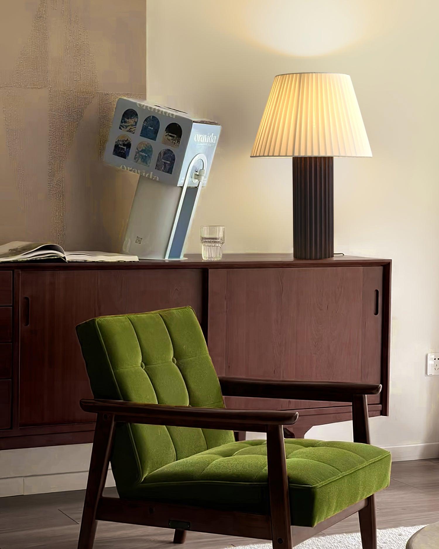 Dark ribbed wooden table lamp with warm lighting in retro mid-century modern living room setting beside green velvet armchair and home furnishings