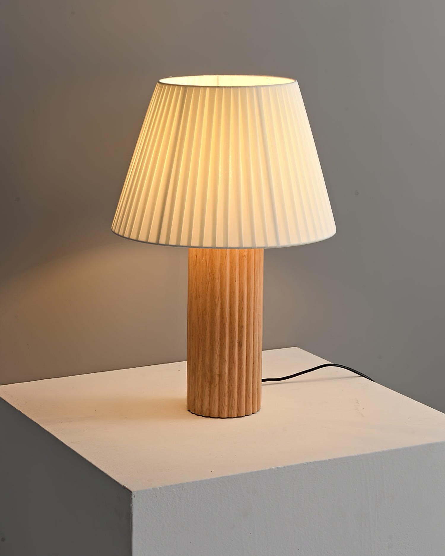 Natural wood grain ribbed base table lamp with warm pleated fabric shade and candle decoration on wall side table in wabi-sabi home style interior