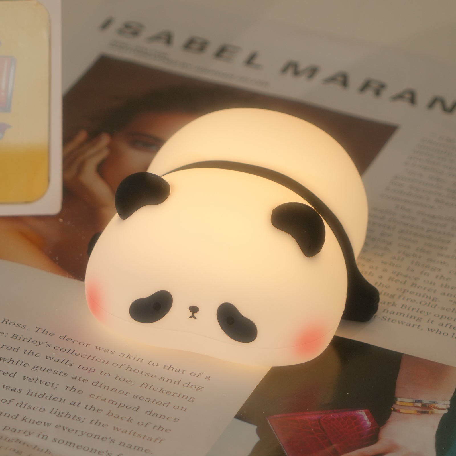 Lying panda night light on tabletop with magazine backdrop - warm ambient glow
