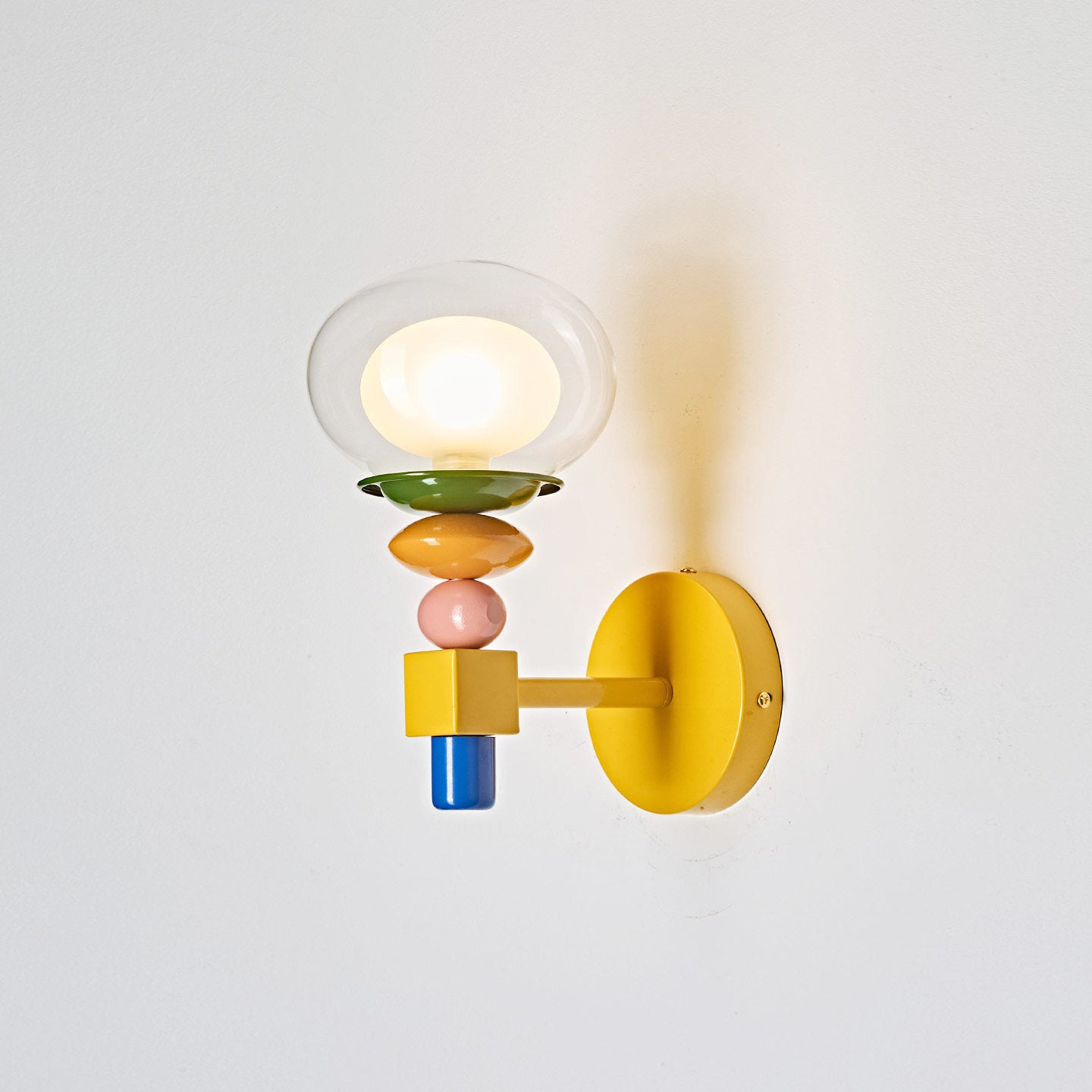 Popella wall sconce side profile showing yellow backplate, stacked color-blocked beads, and illuminated clear glass globe