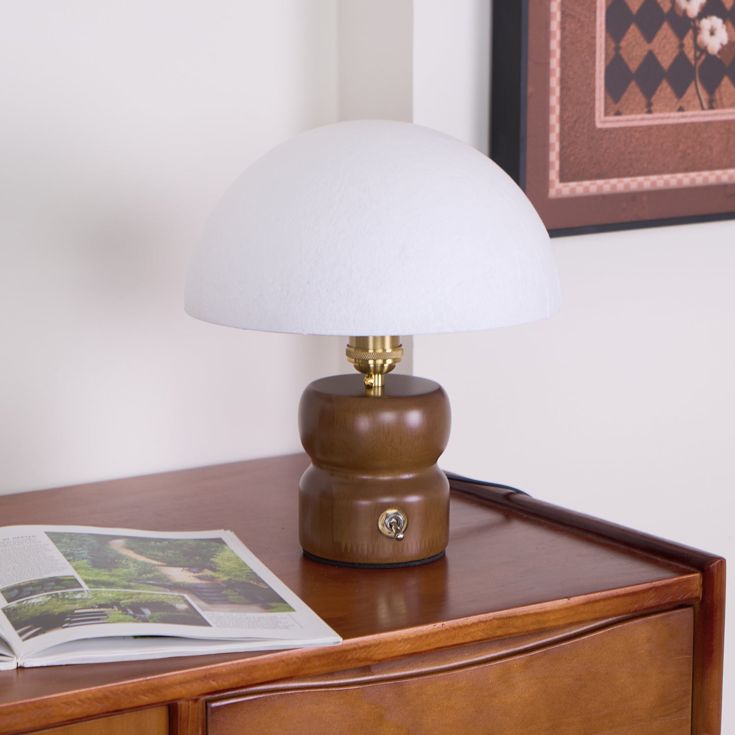 Organic mushroom table lamp with metal toggle switch base on wooden furniture with framed artwork background