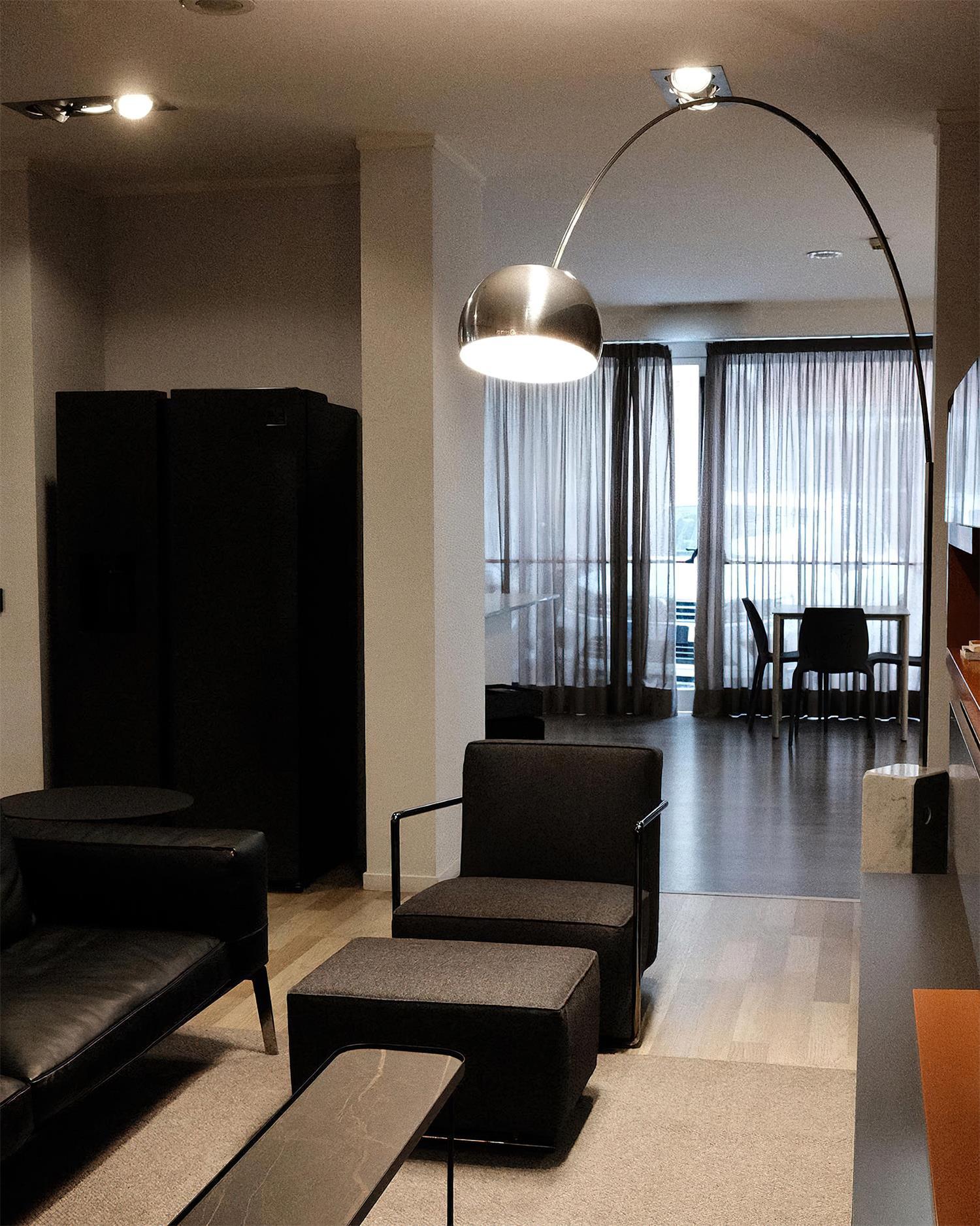 Arc floor lamp with silver fabric shade positioned in dark modern living room corner