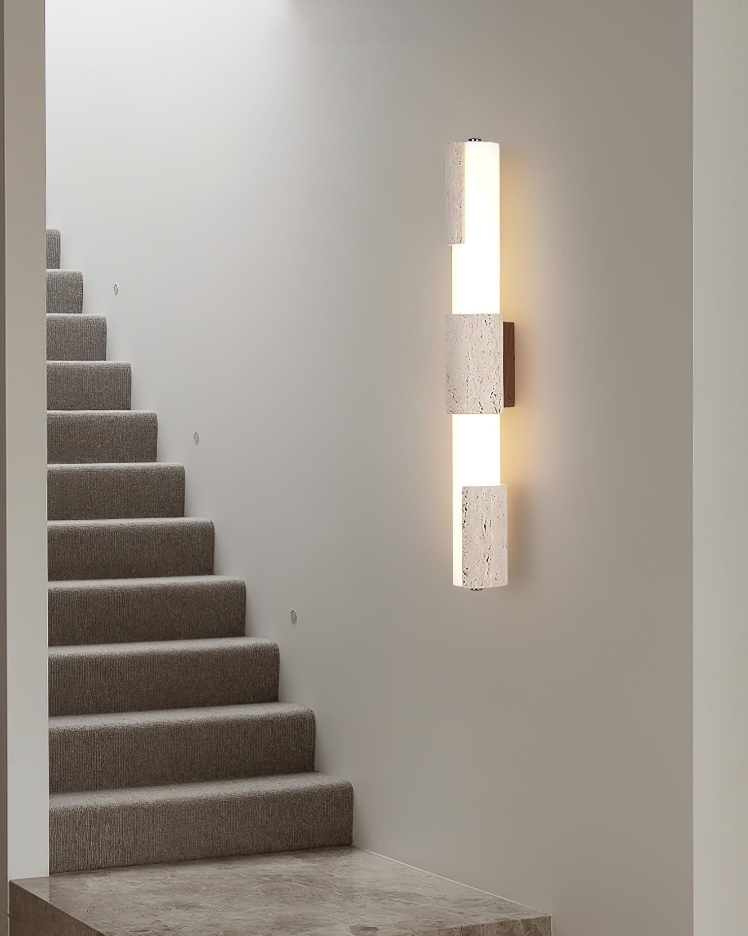Tolira tall travertine wall sconce, 60cm vertical design, front view in minimalist stairwell setting