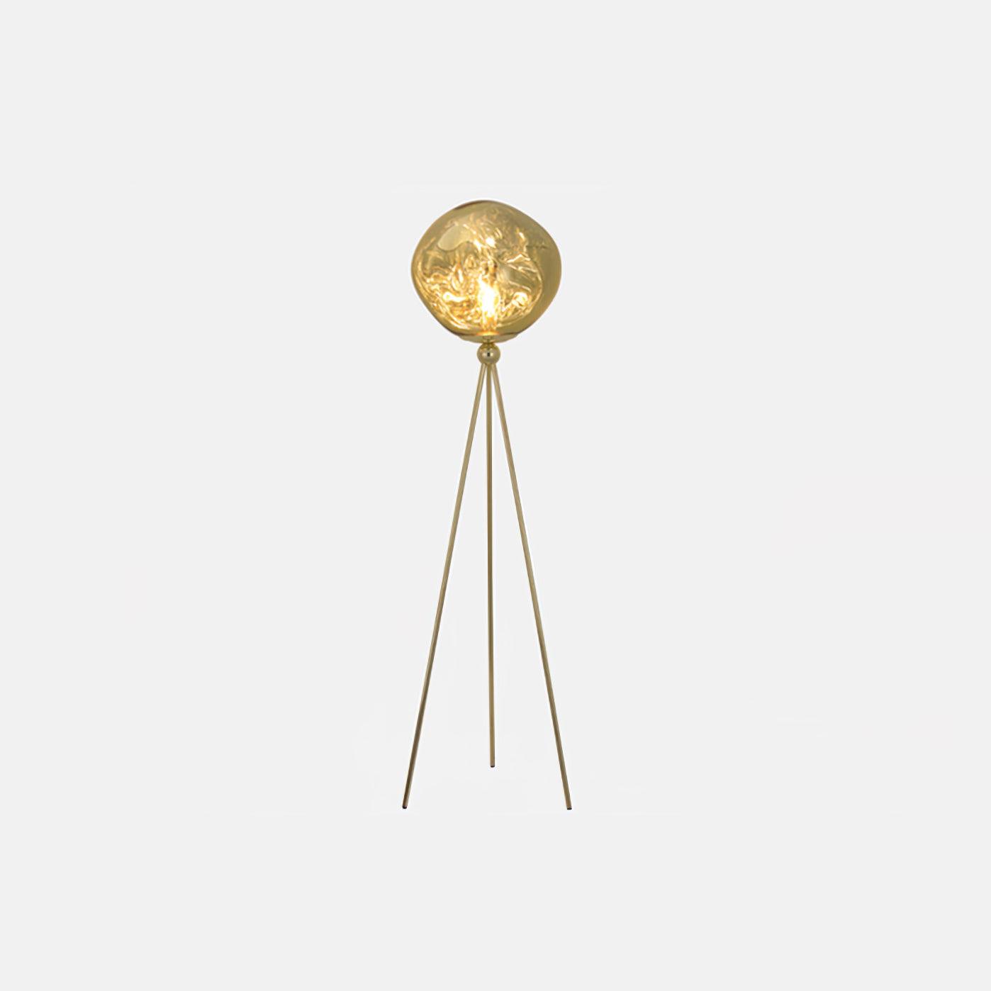 Contemporary gold tripod floor lamp with sculptural molten lava glass shade and warm ambient lighting