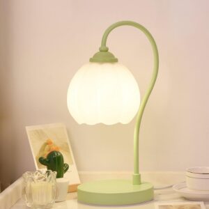 Mint green tulip lamp with warm light glowing on bedroom nightstand with decorative accessories