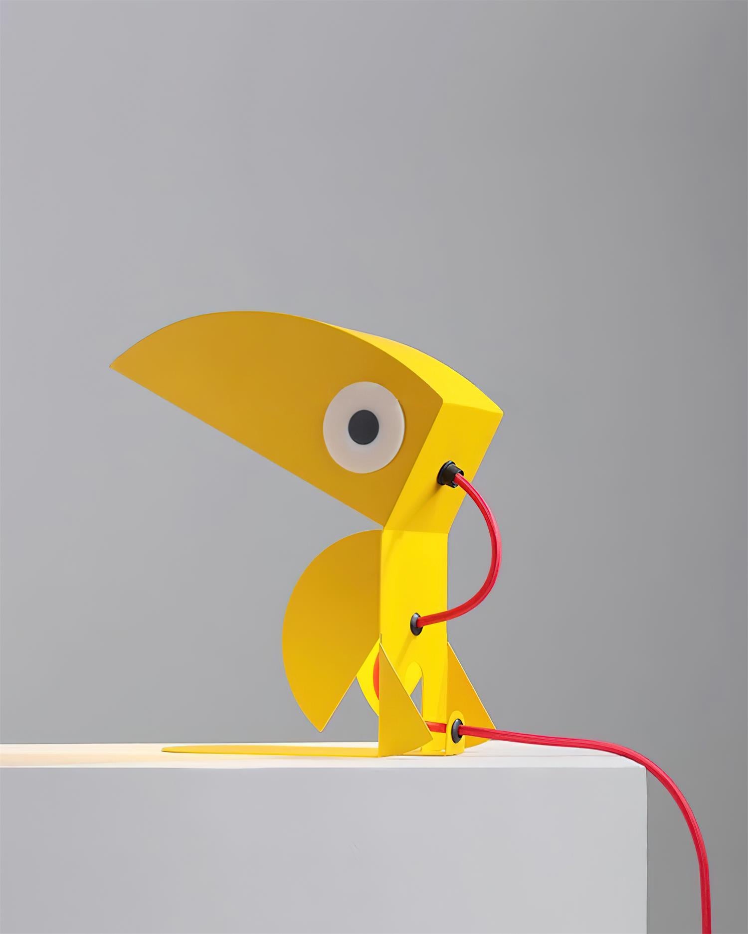Yellow toucan cartoon lamp rear view on minimalist display stand with red power cord