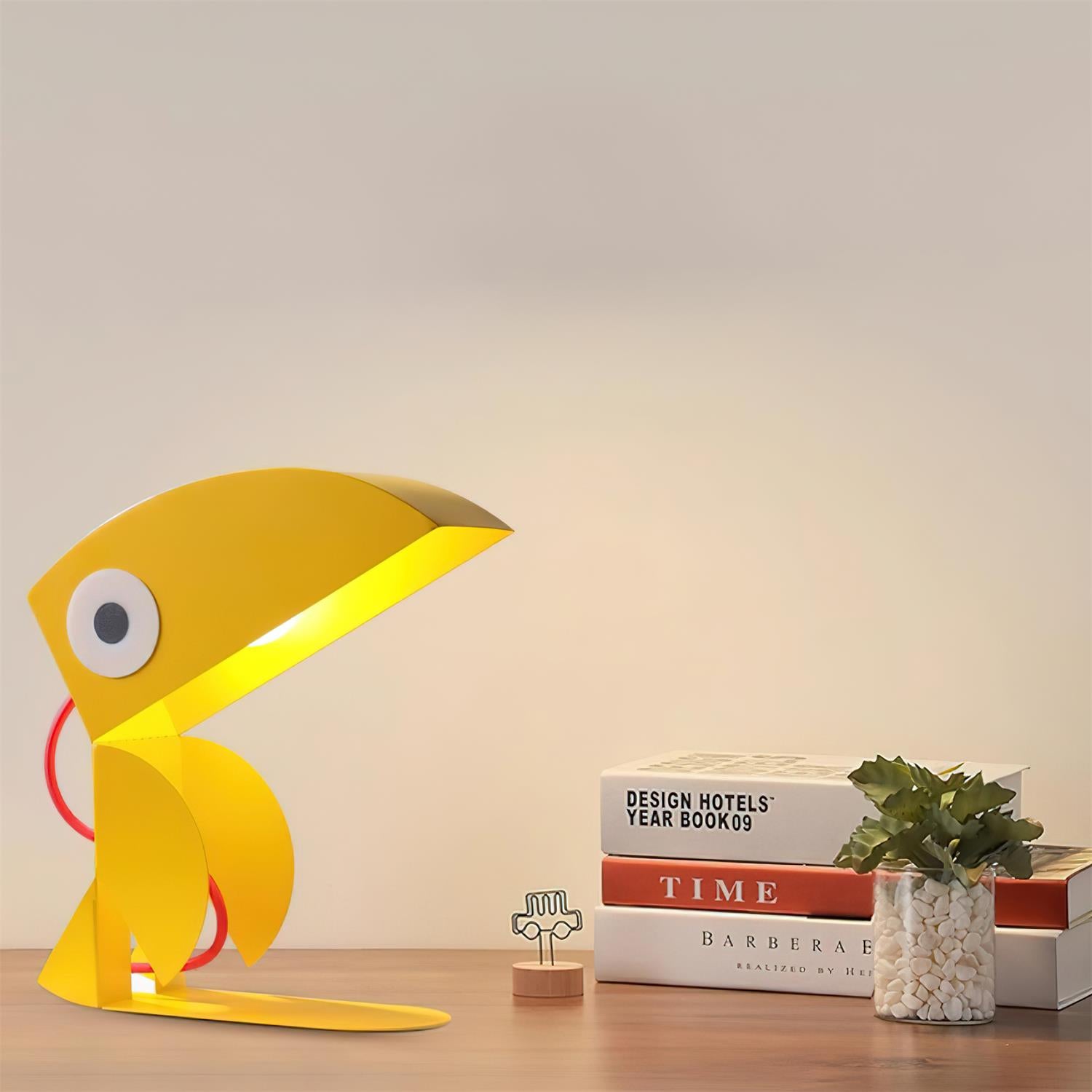 Yellow toucan cartoon table lamp displayed in home office setting with books and plants