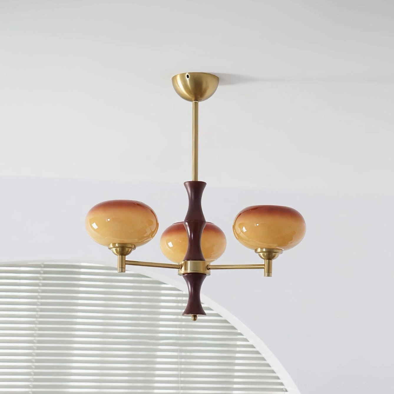 3-head mid-century chandelier with gradient amber-brown glass shades, brass arms, and dark wood stem in home interior with arched louvered window