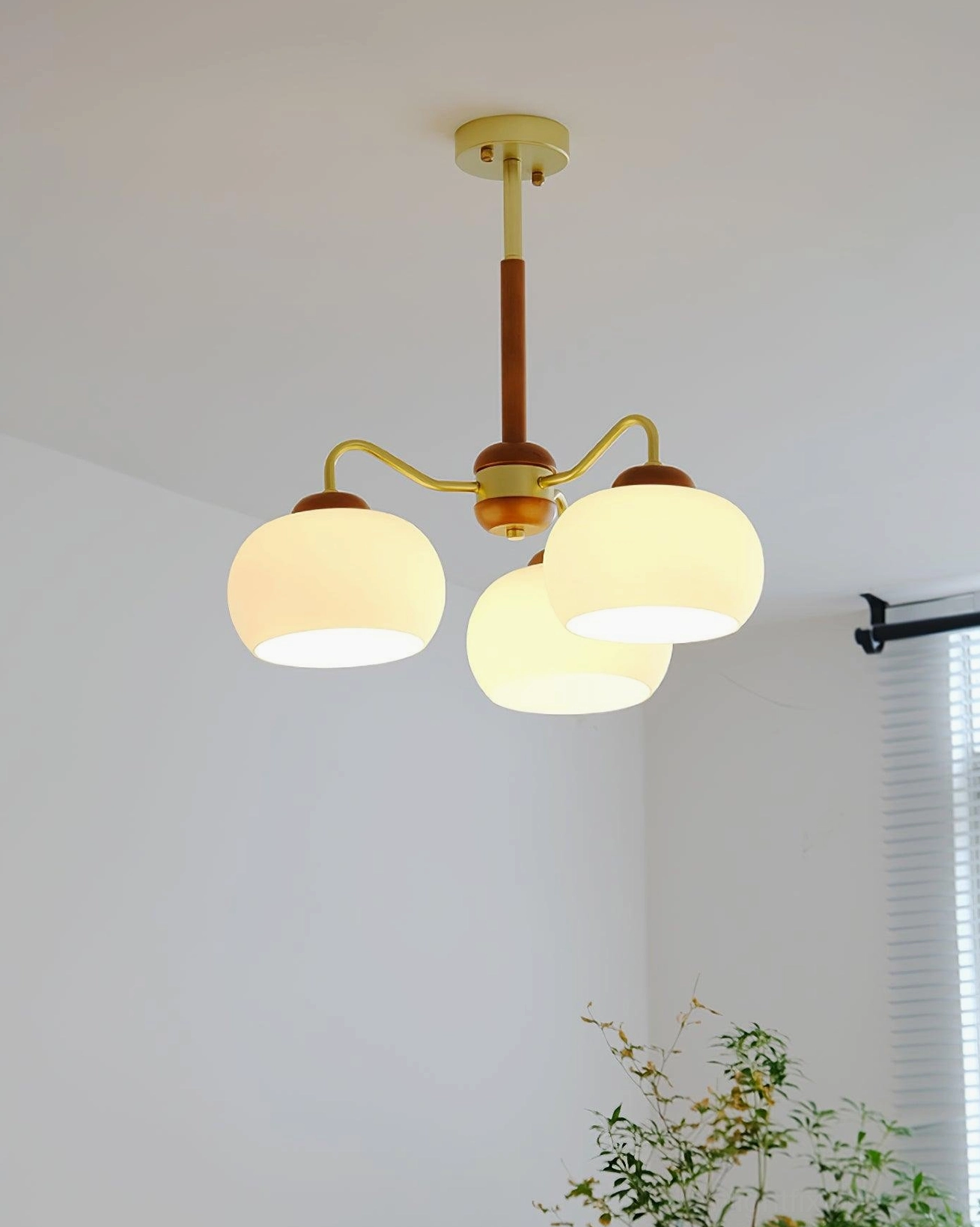 3-light wooden brass chandelier with frosted glass shades lit in residential bedroom with window treatment