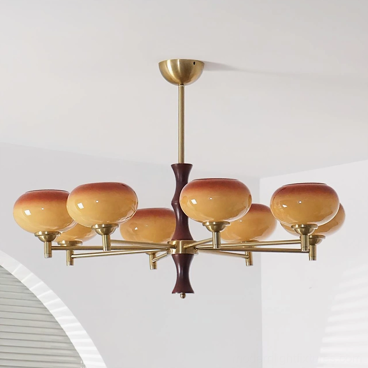 8-head vintage glass chandelier installed in minimalist home interior with arched louvered window, showing warm gradient brown-orange shades and brass hardware