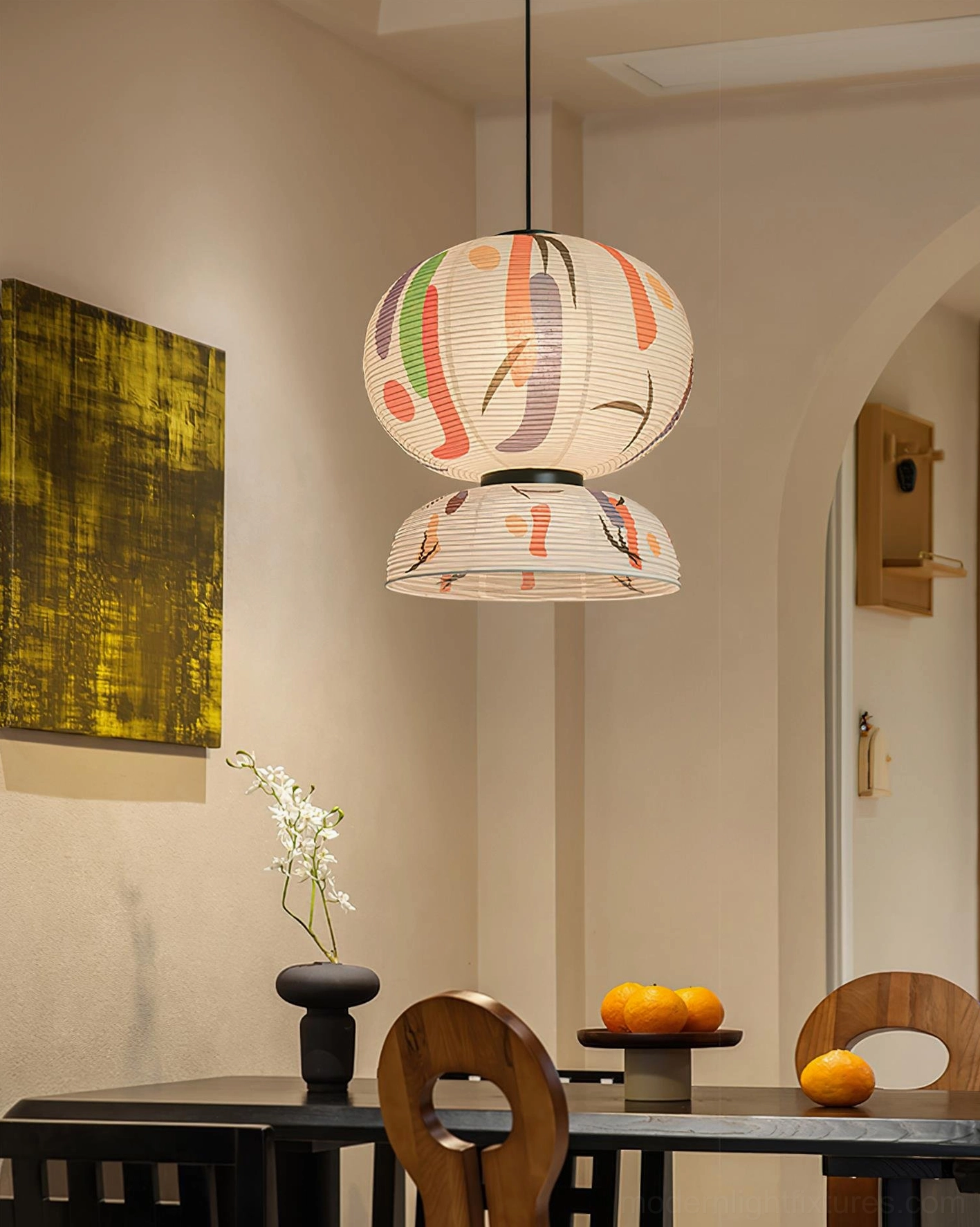 Two-tier abstract printed paper pendant lamp suspended above black dining table with fruit decor in cozy contemporary dining space