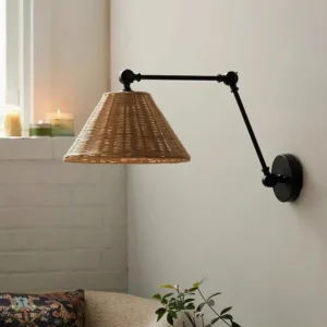 Adjustable swing arm wall sconce with natural rattan shade installed on white brick wall - three-quarter angle