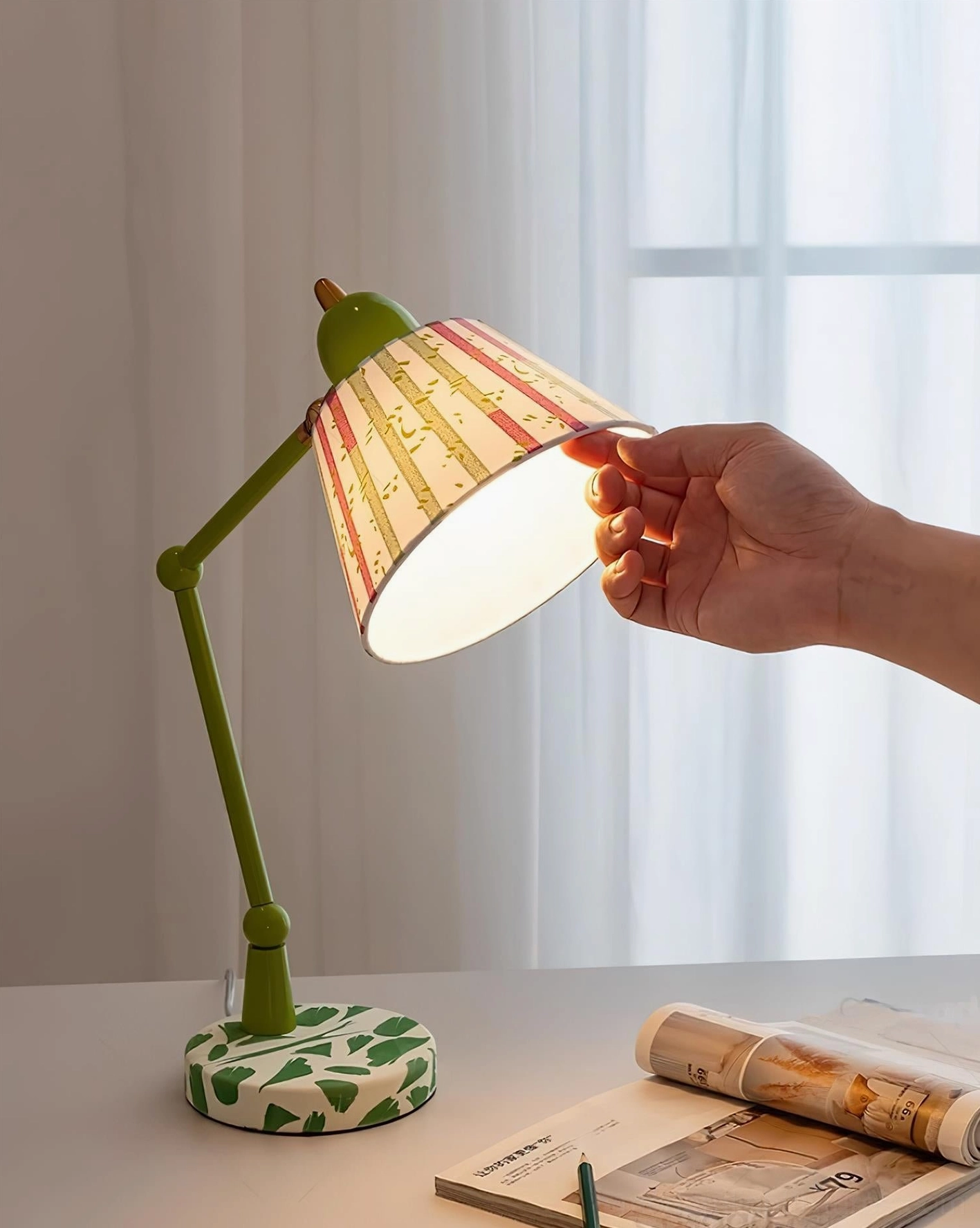 Hand adjusting articulated arm of green table lamp, showing flexibility of swing arm design