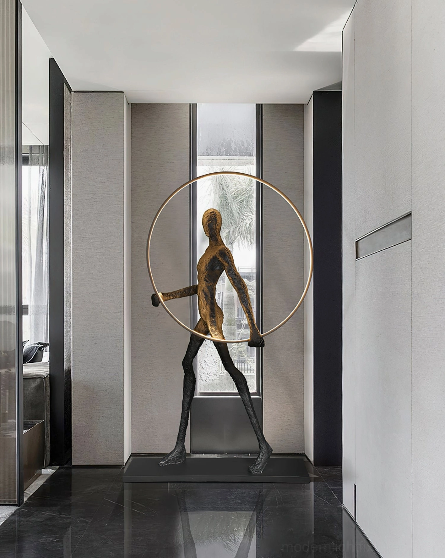 Bronze human sculpture floor lamp with golden warm LED light ring, side profile in hotel lobby corridor