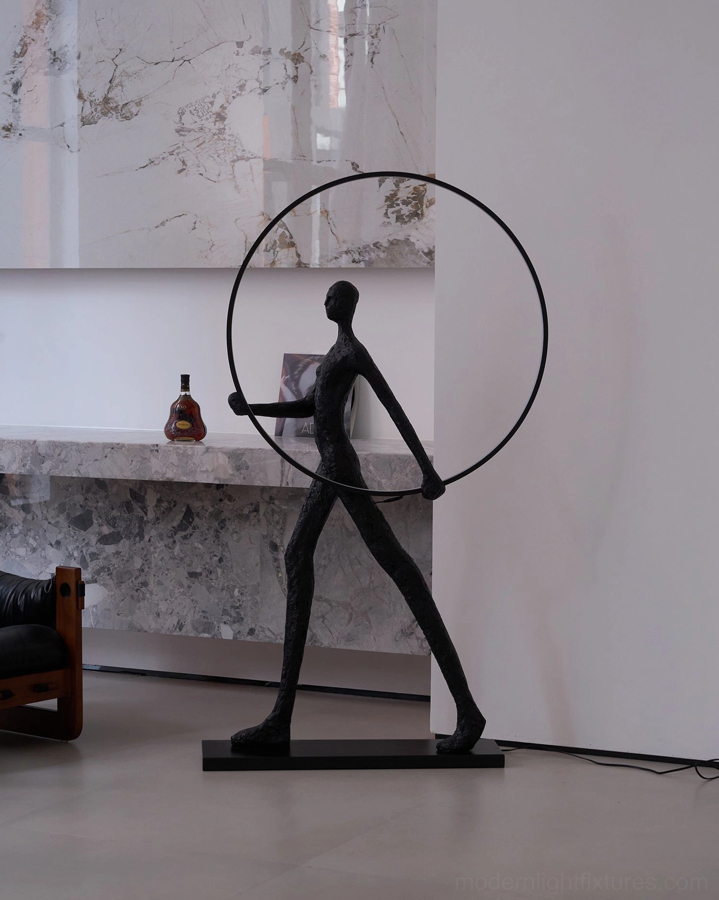 Modern sculptural floor lamp with textured black human form and LED circular frame, rear angle view in marble accent space