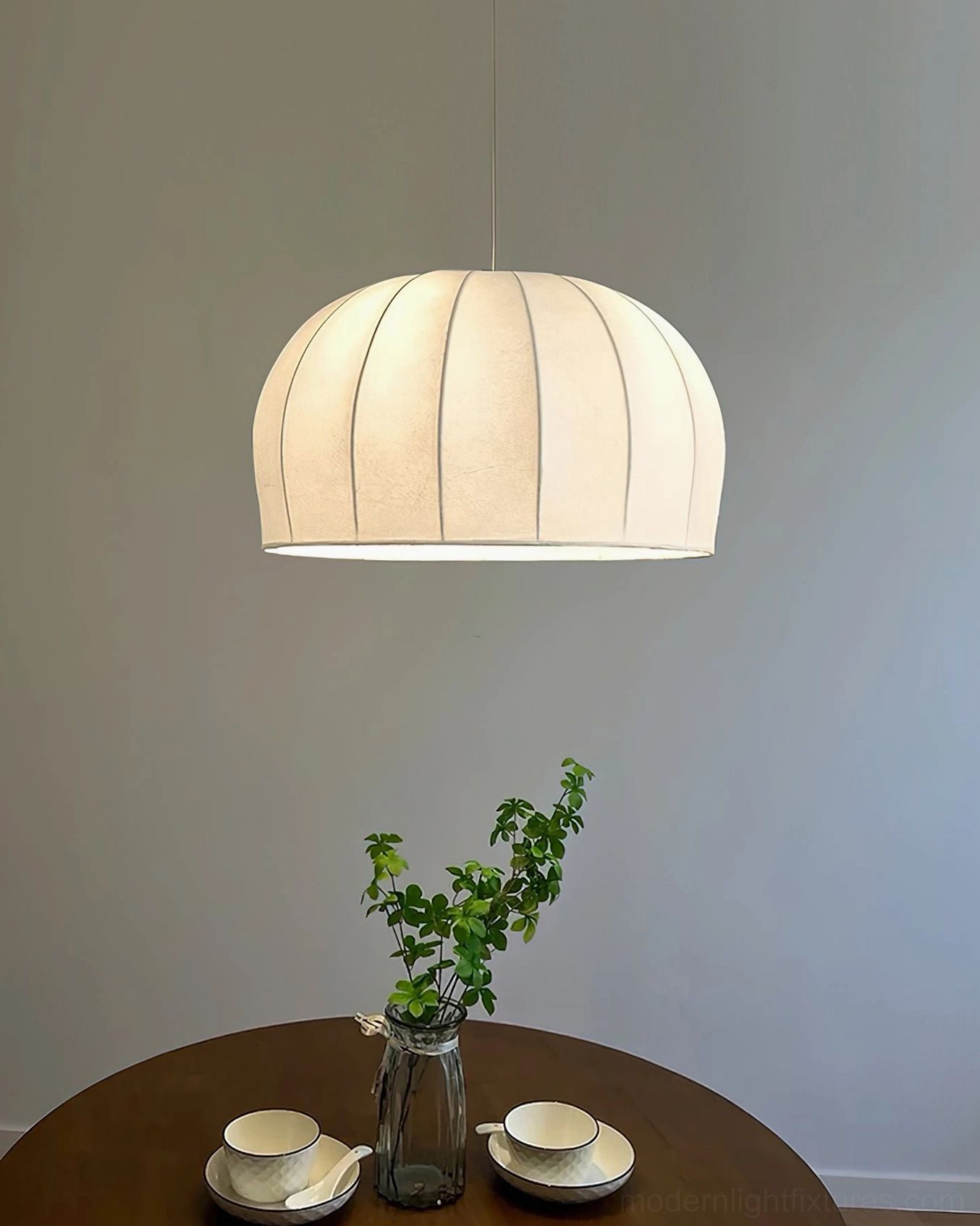 White ribbed fabric pendant light hanging over round wooden dining table, warm neutral interior design