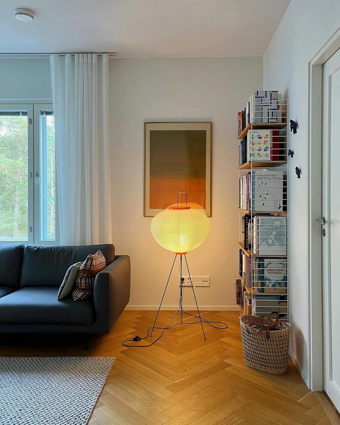 Akari 10A floor lamp in compact Nordic home with dark fabric sofa and wall bookshelf, white lit shade