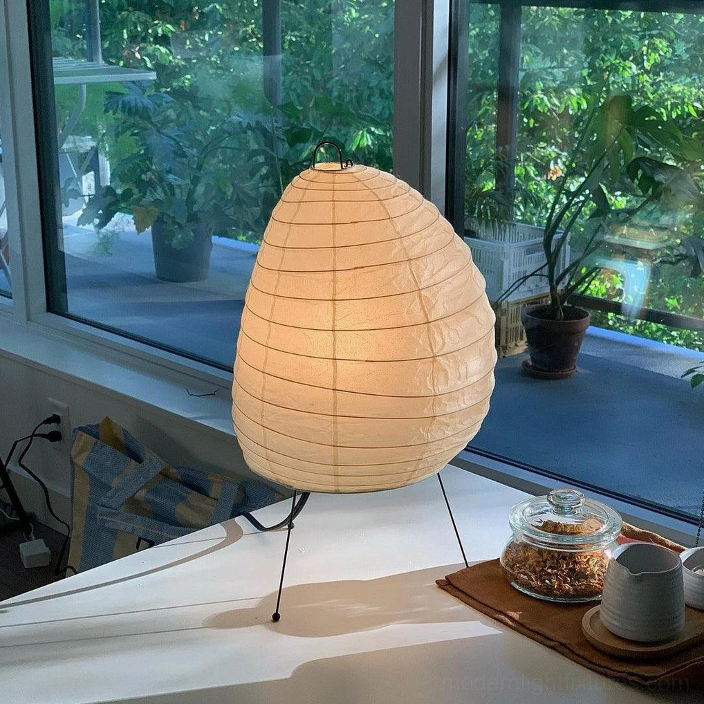 Akari 1N washi paper table lamp illuminated on desk showing warm diffused light and three-quarter view of light diffusion quality
