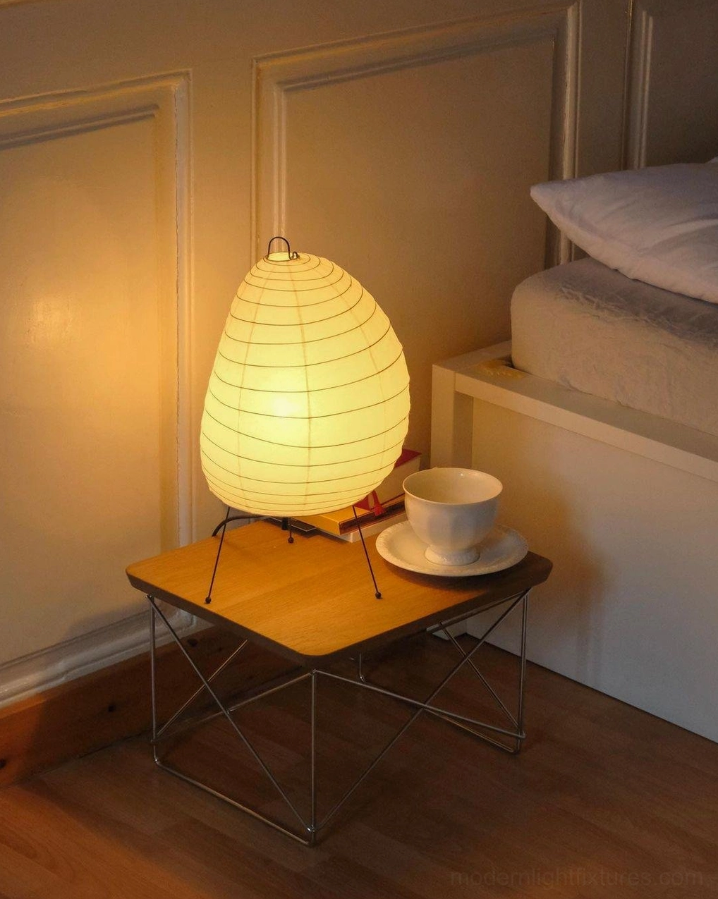 Akari 1N washi paper diffused light lamp on wooden side table with tea cup set against paneled wall in cozy bedroom