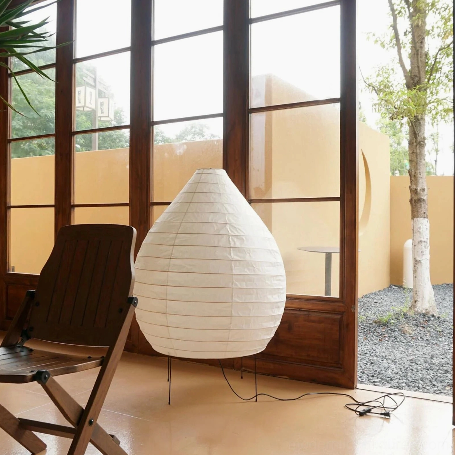 Akari 23N teardrop floor lamp three-quarter side view on residential patio with black metal tripod base