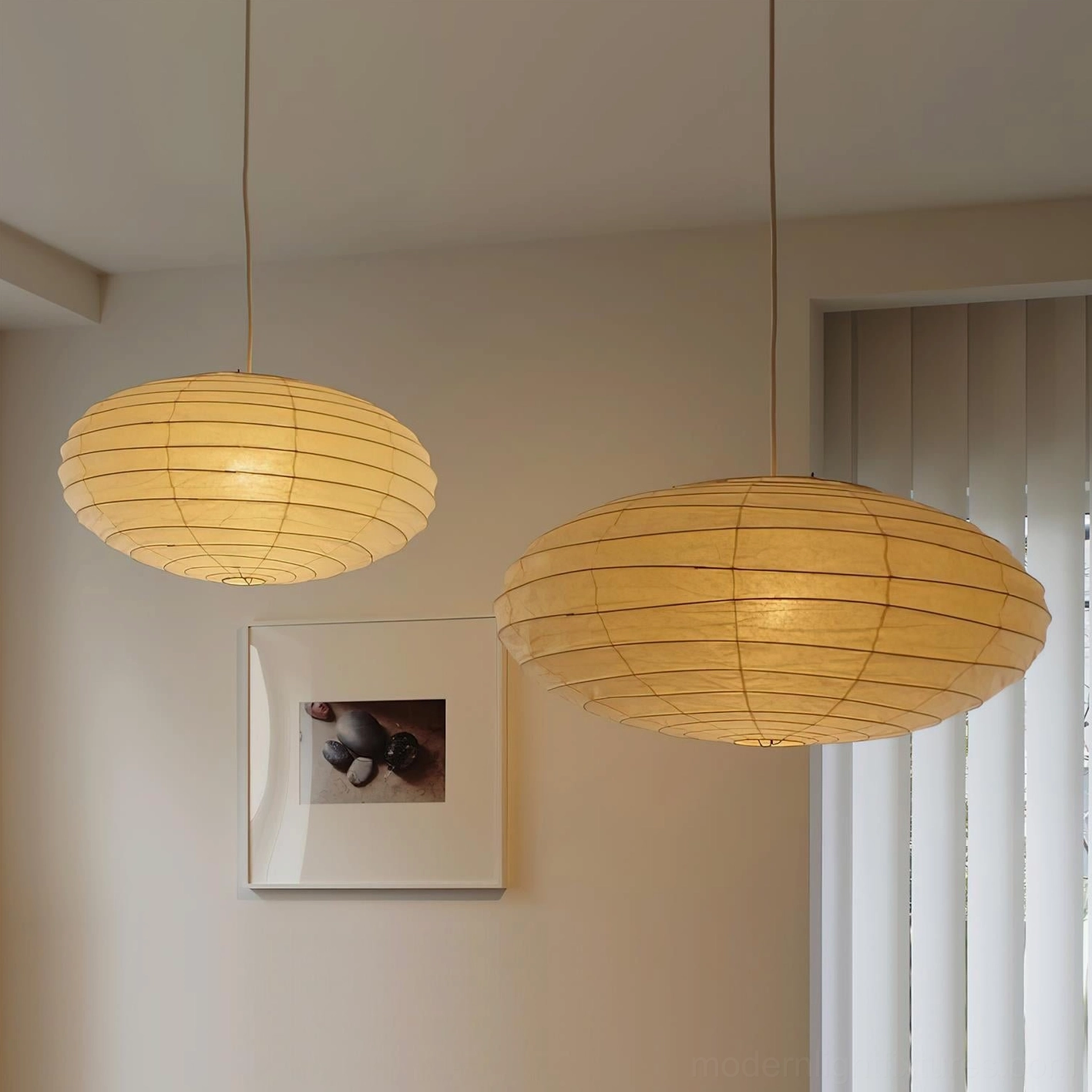 Two Akari 50EN illuminated washi paper pendant lamps hanging in minimalist home hallway with wall artwork, warm beige glow