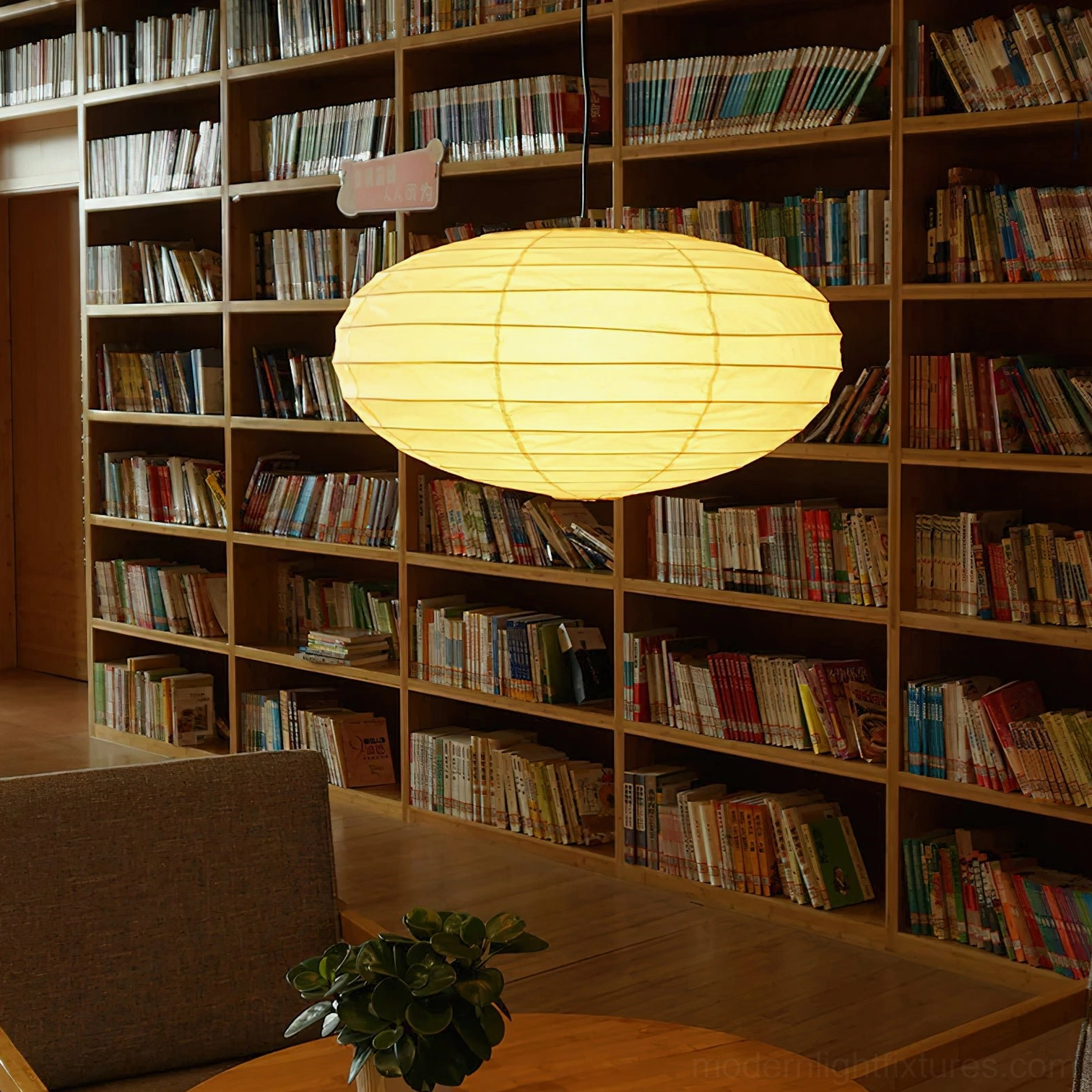 Akari 50EN large pendant lamp illuminated in bookstore café lounge area, emitting warm yellow light with bookshelf background