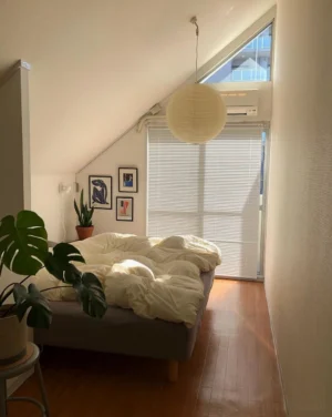 Japanese Akari A pendant light hanging above bed in bedroom with sloped ceiling