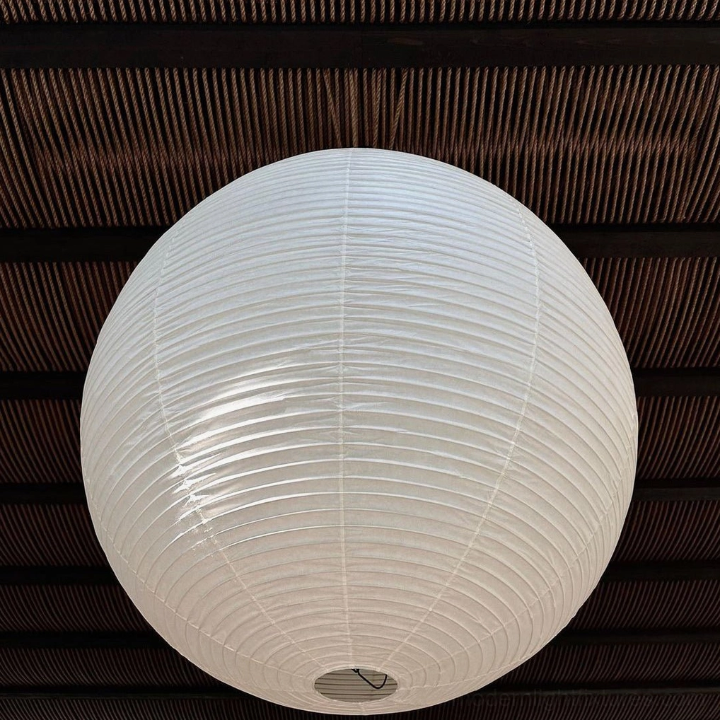 Close-up view of white ribbed Akari A pendant shade with dark slatted ceiling