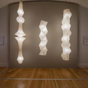 Modern white Akari E pendant lamp hanging in minimalist living room with wood flooring and warm ambient lighting
